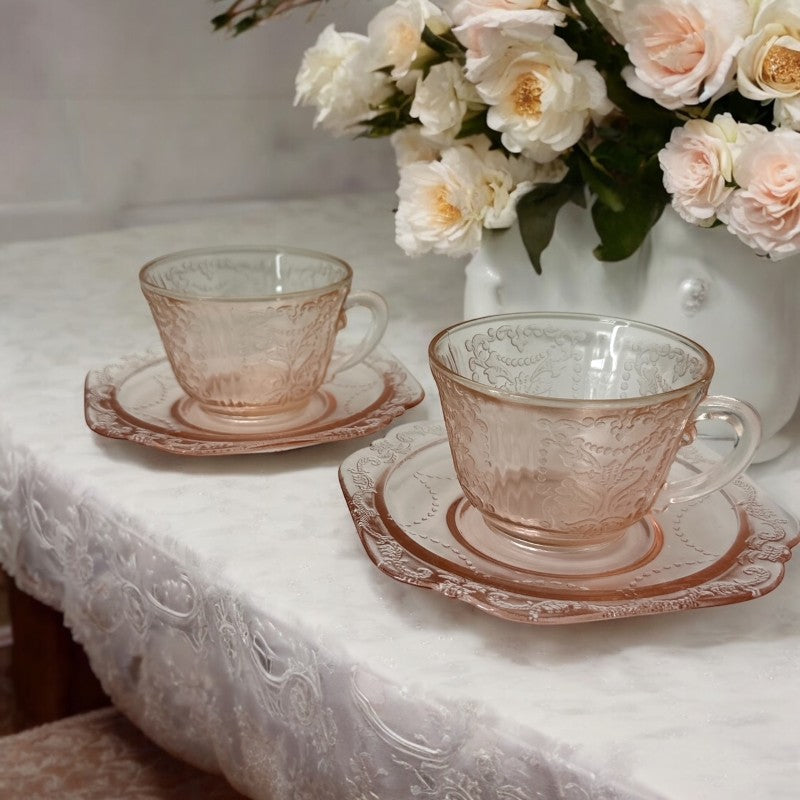 Vintage pink depression glass set featuring 2 delicate cups from the American Sweetheart collection and 2 square saucers from the Madrid collection, both adorned with intricate floral and geometric etched patterns. A timeless and sustainable addition to any table or décor.