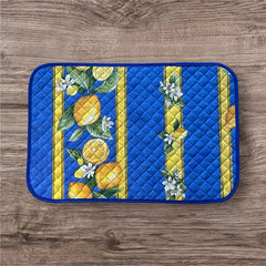 Reversible quilted cotton placemat in Lemons Blue by Tissus Toselli, featuring a blue background with vertical lemon garlands, green leaves, and white blossoms framed by golden diamond borders, identical on both sides, made in Provence."