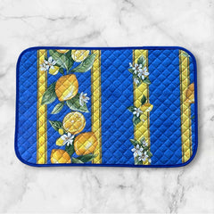 Reversible quilted cotton placemat in Lemons Blue by Tissus Toselli, featuring a blue background with vertical lemon garlands, green leaves, and white blossoms framed by golden diamond borders, identical on both sides, made in Provence."