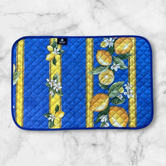 Reversible quilted cotton placemat in Lemons Blue by Tissus Toselli, featuring a blue background with vertical lemon garlands, green leaves, and white blossoms framed by golden diamond borders, identical on both sides, made in Provence."