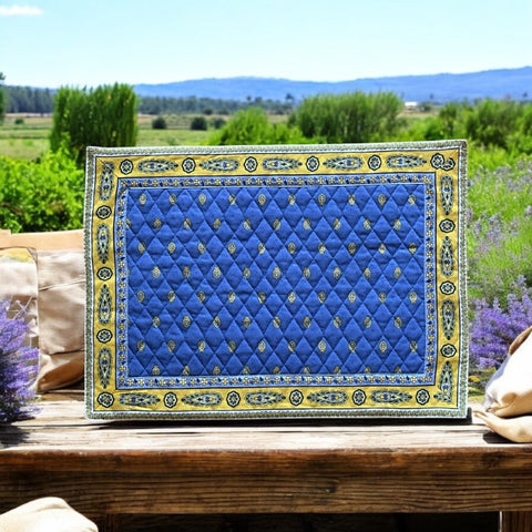 Reversible quilted cotton placemat in Bastide Blue Yellow by Marat d’Avignon, featuring a bold blue floral diamond motif with yellow paisley borders on the front, and a blue background with golden yellow medallions on the reverse, crafted in Provence.
