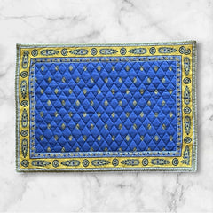 Reversible quilted cotton placemat in Bastide Blue Yellow by Marat d’Avignon, featuring a bold blue floral diamond motif with yellow paisley borders on the front, and a blue background with golden yellow medallions on the reverse, crafted in Provence.