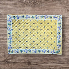 Reversible quilted cotton placemat in Lauris Light Yellow by Marat d’Avignon, featuring a pale yellow center with blue floral medallions and a border of lavender sprigs and olive branches, with a reverse side of soft yellow scattered with tiny blue and white blossoms, crafted in Provence.