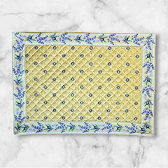 Reversible quilted cotton placemat in Lauris Light Yellow by Marat d’Avignon, featuring a pale yellow center with blue floral medallions and a border of lavender sprigs and olive branches, with a reverse side of soft yellow scattered with tiny blue and white blossoms, crafted in Provence.