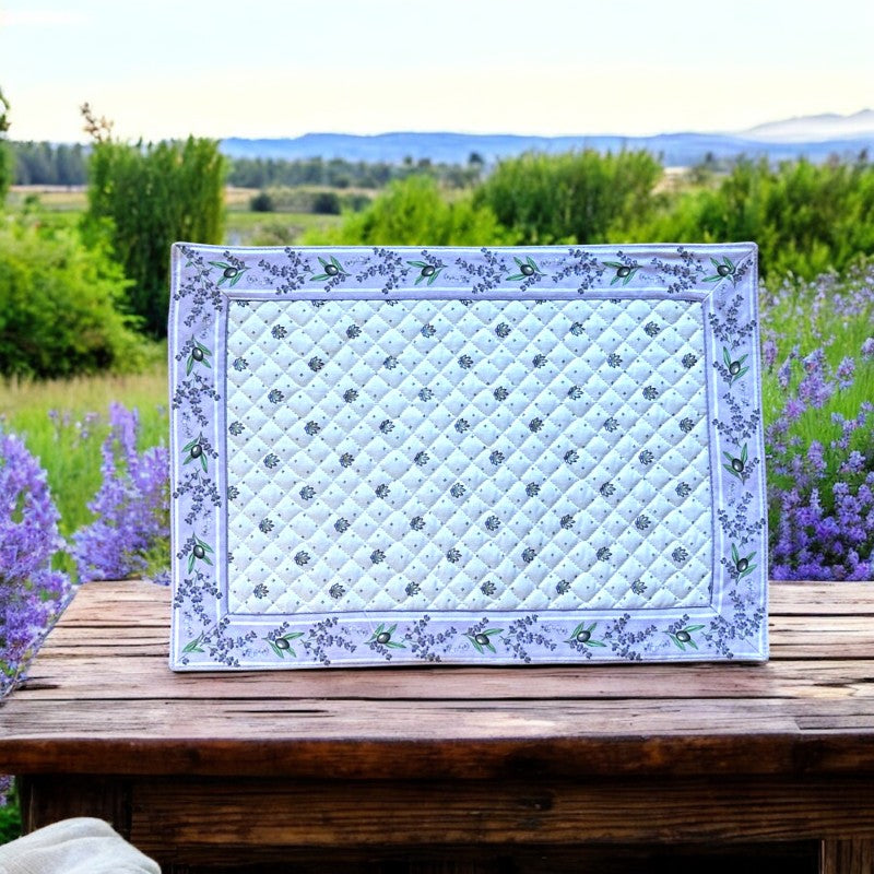 Reversible quilted cotton placemat in Lauris Light Yellow by Marat d’Avignon, featuring a white center with lavender purple floral medallions and a border of lavender sprigs and olive branches, with a white reverse side  scattered with tiny lavender  blossoms, crafted in Provence.