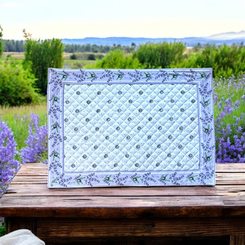 Reversible quilted cotton placemat in Lauris Light Yellow by Marat d’Avignon, featuring a white center with lavender purple floral medallions and a border of lavender sprigs and olive branches, with a white reverse side  scattered with tiny lavender  blossoms, crafted in Provence.