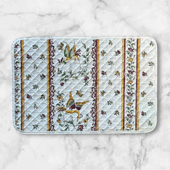Provence Reversible quilted cotton placemat in Moustiers Red by Tissus Toselli, featuring traditional Provençal motifs inspired by Moustiers ceramics, with two birds in flight, floral garlands, and cream trim.