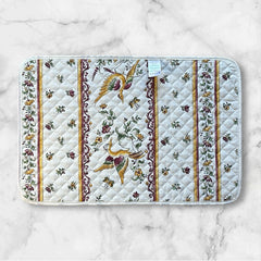 Provence Reversible quilted cotton placemat in Moustiers Red by Tissus Toselli, featuring traditional Provençal motifs inspired by Moustiers ceramics, with two birds in flight, floral garlands, and cream trim.