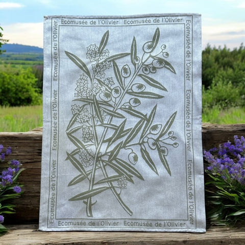 Provence tea towel featuring an olive branch with fruits and flowers at the center, framed by the repeated text 'L'Écomusée de l'Olivier.' Woven in olive green on a natural background with a 100% cotton composition, blending rustic charm and elegance.