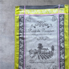 French Provence tea towel featuring the Rosé de Provence Appellation Contrôlée design, showcasing a vineyard and winery in elegant cotton. Available in orange with yellow accents and green with soft purple and gray details. Decorative and eco-friendly kitchen decor.