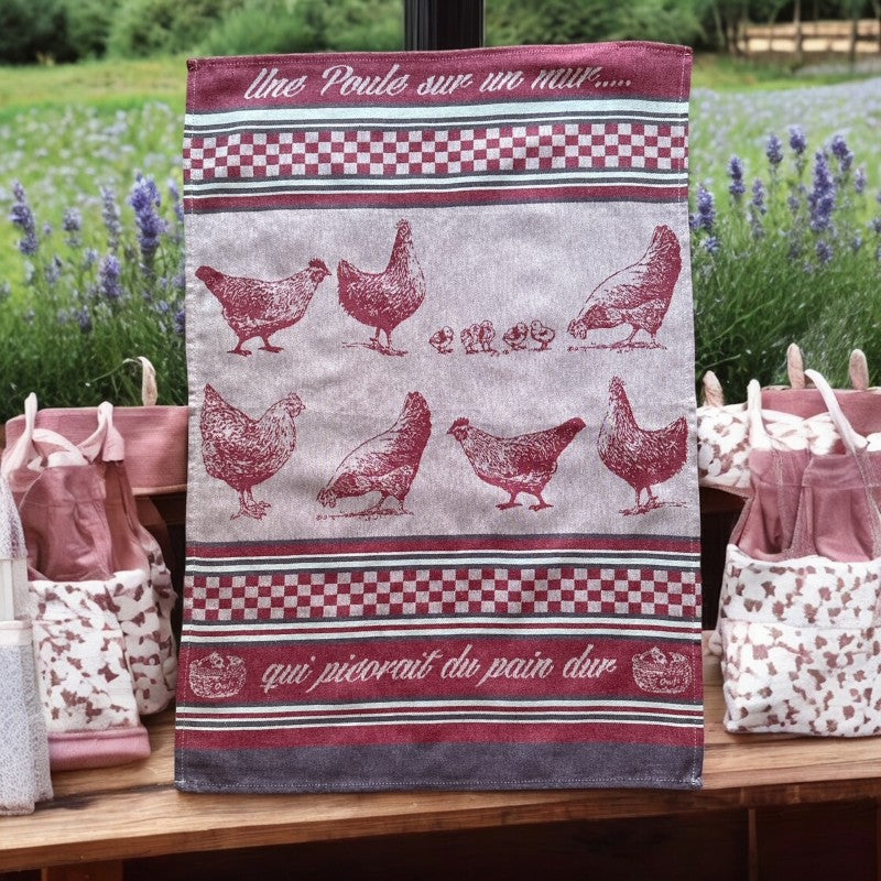Provence tea towel featuring a Poule design with hens and chicks, woven in red and natural tones with eggplant-colored stripes and a checkered pattern. Includes the French children's song 'Une poule sur un mur qui picorait du pain dur.' Made of 100% cotton, perfect for decorative kitchen use.