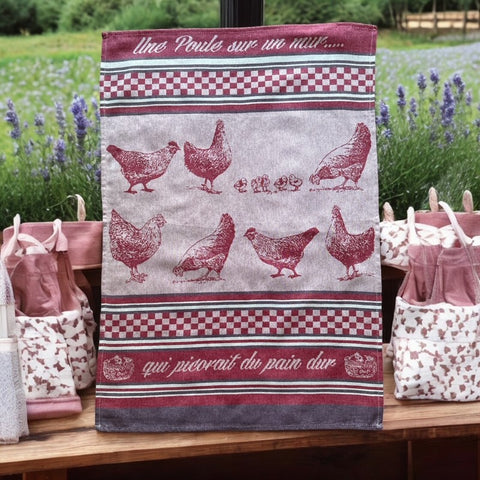 Provence tea towel featuring a Poule design with hens and chicks, woven in red and natural tones with eggplant-colored stripes and a checkered pattern. Includes the French children's song 'Une poule sur un mur qui picorait du pain dur.' Made of 100% cotton, perfect for decorative kitchen use.