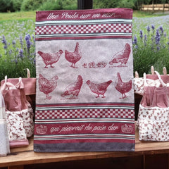 Provence tea towel featuring a Poule design with hens and chicks, woven in red and natural tones with eggplant-colored stripes and a checkered pattern. Includes the French children's song 'Une poule sur un mur qui picorait du pain dur.' Made of 100% cotton, perfect for decorative kitchen use.