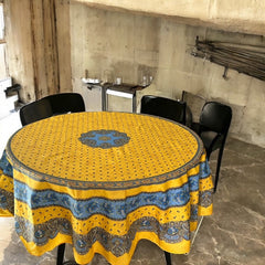 Round Provence-style coated cotton tablecloth by Marat d'Avignon, featuring a vibrant yellow background with blue and white floral patterns. Measures 70 inches in diameter, perfect for indoor and outdoor use, and easy to clean.