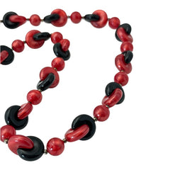 A vintage necklace featuring marbleized red and shiny black plastic beads from the 1990s. The design includes interlocking red and black donut-shaped beads with a round marbleized red bead between each combination. A bold and artistic statement accessory in very good vintage condition.