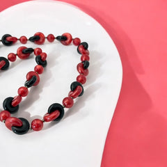 A vintage necklace featuring marbleized red and shiny black plastic beads from the 1990s. The design includes interlocking red and black donut-shaped beads with a round marbleized red bead between each combination. A bold and artistic statement accessory in very good vintage condition.