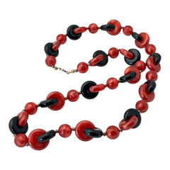 A vintage necklace featuring marbleized red and shiny black plastic beads from the 1990s. The design includes interlocking red and black donut-shaped beads with a round marbleized red bead between each combination. A bold and artistic statement accessory in very good vintage condition.