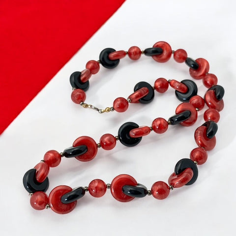 A vintage necklace featuring marbleized red and shiny black plastic beads from the 1990s. The design includes interlocking red and black donut-shaped beads with a round marbleized red bead between each combination. A bold and artistic statement accessory in very good vintage condition.