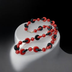 A vintage necklace featuring marbleized red and shiny black plastic beads from the 1990s. The design includes interlocking red and black donut-shaped beads with a round marbleized red bead between each combination. A bold and artistic statement accessory in very good vintage condition.