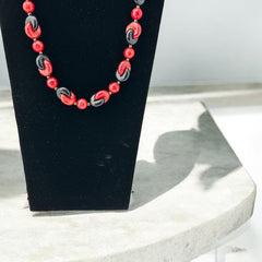 A vintage necklace featuring marbleized red and shiny black plastic beads from the 1990s. The design includes interlocking red and black donut-shaped beads with a round marbleized red bead between each combination. A bold and artistic statement accessory in very good vintage condition.