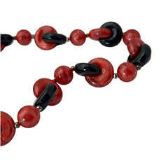 A vintage necklace featuring marbleized red and shiny black plastic beads from the 1990s. The design includes interlocking red and black donut-shaped beads with a round marbleized red bead between each combination. A bold and artistic statement accessory in very good vintage condition.