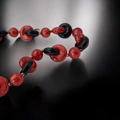 A vintage necklace featuring marbleized red and shiny black plastic beads from the 1990s. The design includes interlocking red and black donut-shaped beads with a round marbleized red bead between each combination. A bold and artistic statement accessory in very good vintage condition.