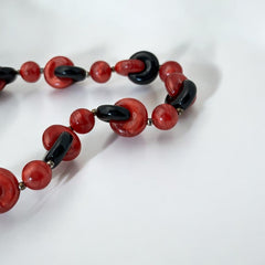 A vintage necklace featuring marbleized red and shiny black plastic beads from the 1990s. The design includes interlocking red and black donut-shaped beads with a round marbleized red bead between each combination. A bold and artistic statement accessory in very good vintage condition.