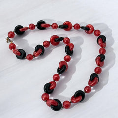 A vintage necklace featuring marbleized red and shiny black plastic beads from the 1990s. The design includes interlocking red and black donut-shaped beads with a round marbleized red bead between each combination. A bold and artistic statement accessory in very good vintage condition.