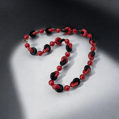 A vintage necklace featuring marbleized red and shiny black plastic beads from the 1990s. The design includes interlocking red and black donut-shaped beads with a round marbleized red bead between each combination. A bold and artistic statement accessory in very good vintage condition.
