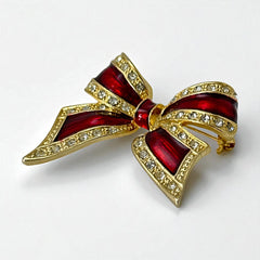 Vintage 1990s bow brooch in red enamel and gold-tone metal with pavé rhinestones, shown worn or displayed to highlight its elegant design and excellent condition.