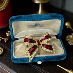 Vintage 1990s bow brooch in red enamel and gold-tone metal with pavé rhinestones, shown worn or displayed to highlight its elegant design and excellent condition.