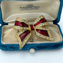Vintage 1990s bow brooch in red enamel and gold-tone metal with pavé rhinestones, shown worn or displayed to highlight its elegant design and excellent condition.