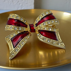 Vintage 1990s bow brooch in red enamel and gold-tone metal with pavé rhinestones, shown worn or displayed to highlight its elegant design and excellent condition.