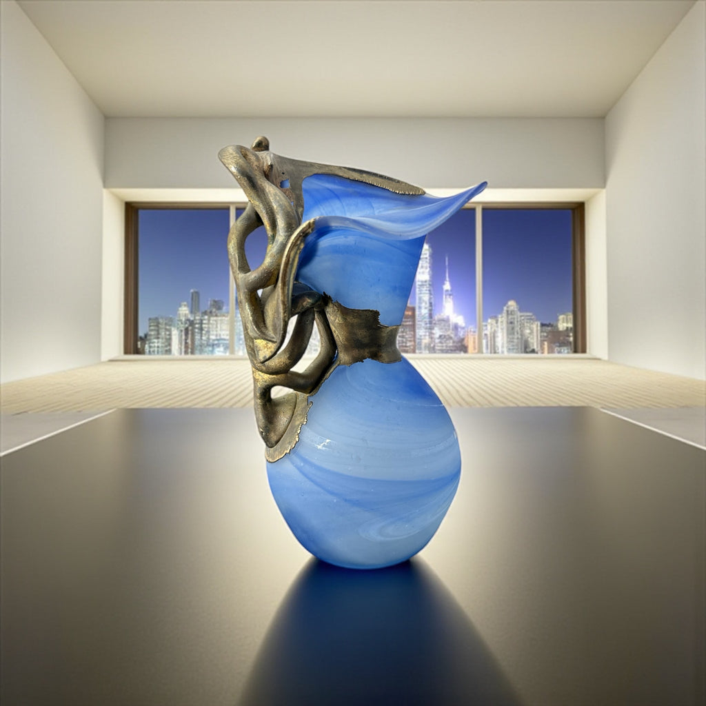 Signed Romanian handblown art glass vase from the 1990s featuring swirling blue glass and sculptural bronze overlay with organic vine-like forms. The vase has a flared top, narrow base, and an undeciphered artist’s signature etched into the glass. A collectible decorative piece in very good vintage condition.