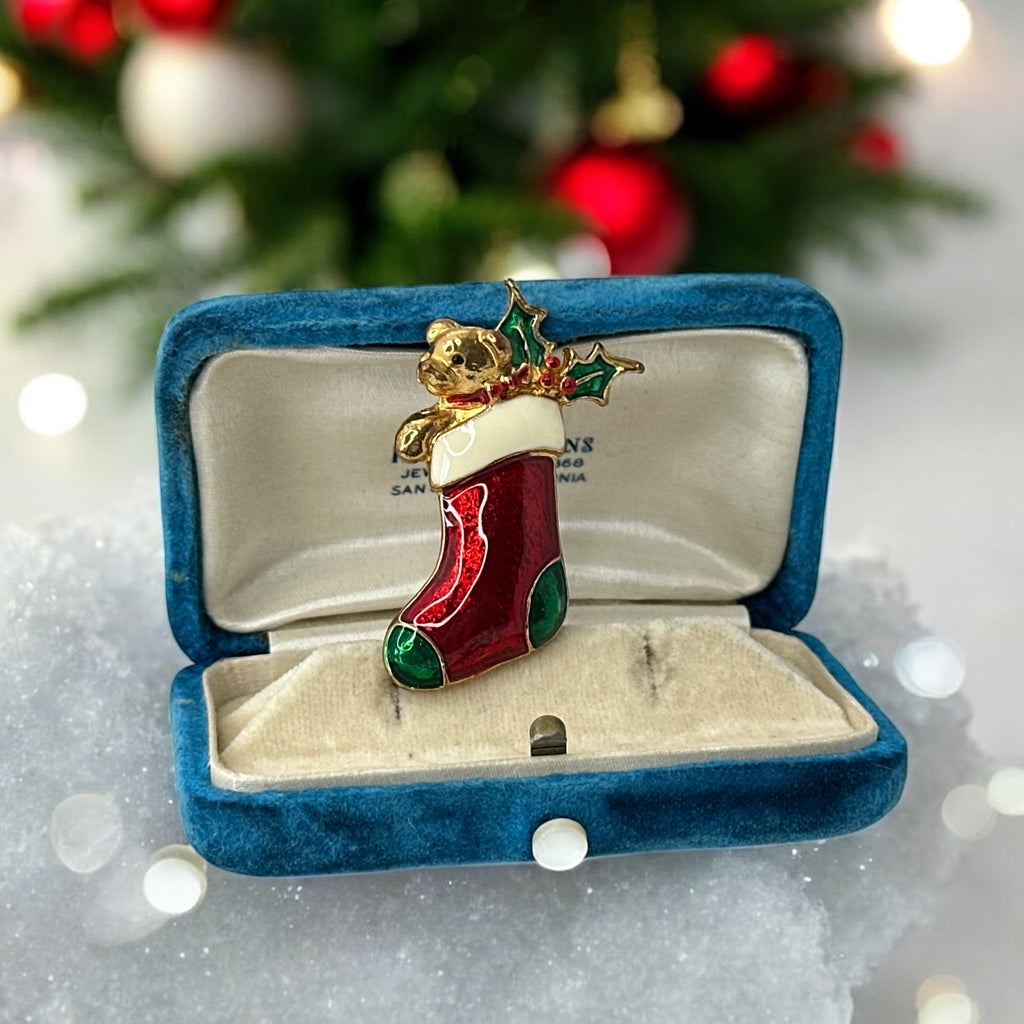Vintage SFJ Christmas stocking brooch in gold tone metal with red, green, and white enamel; features teddy bear and holly details, signed SFJ on back.