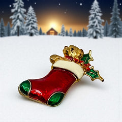 Vintage SFJ Christmas stocking brooch in gold tone metal with red, green, and white enamel; features teddy bear and holly details, signed SFJ on back.