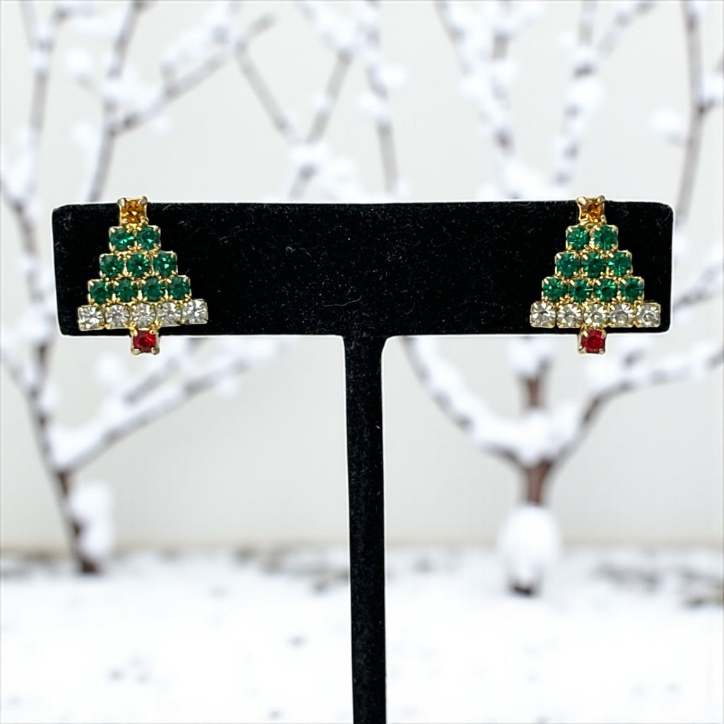 Pair of vintage Sarah Coventry clip-on earrings shaped like Christmas trees, featuring clear and green rhinestones as leaves, a red rhinestone trunk, and a yellow rhinestone star at the top. Gold tone metal with signed clips. Small size, festive design.