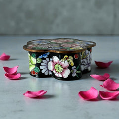 Vintage Seymour Mann flower-shaped trinket box with black enamel exterior, decorated with multicolored floral designs outlined in gold; features a light blue enamel interior and sculpted petal edges.