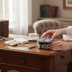 Vintage Seymour Mann flower-shaped trinket box with black enamel exterior, decorated with multicolored floral designs outlined in gold; features a light blue enamel interior and sculpted petal edges.