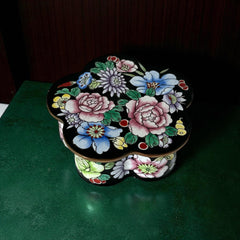 Vintage Seymour Mann flower-shaped trinket box with black enamel exterior, decorated with multicolored floral designs outlined in gold; features a light blue enamel interior and sculpted petal edges.