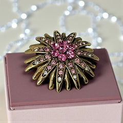 Vintage sunburst brooch with pink and clear rhinestones set in gold tone metal, featuring pointed petal-like rays and a central cluster of pink stones, photographed front and back to highlight its 1980s design and secure clasp.