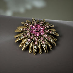 Vintage sunburst brooch with pink and clear rhinestones set in gold tone metal, featuring pointed petal-like rays and a central cluster of pink stones, photographed front and back to highlight its 1980s design and secure clasp.