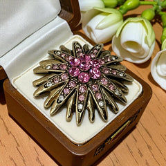 Vintage sunburst brooch with pink and clear rhinestones set in gold tone metal, featuring pointed petal-like rays and a central cluster of pink stones, photographed front and back to highlight its 1980s design and secure clasp.