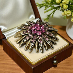 Vintage sunburst brooch with pink and clear rhinestones set in gold tone metal, featuring pointed petal-like rays and a central cluster of pink stones, photographed front and back to highlight its 1980s design and secure clasp.