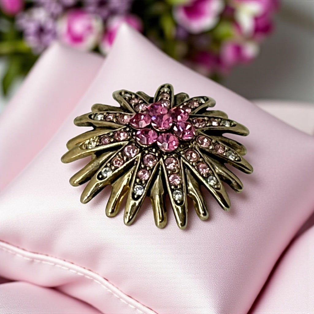 Vintage sunburst brooch with pink and clear rhinestones set in gold tone metal, featuring pointed petal-like rays and a central cluster of pink stones, photographed front and back to highlight its 1980s design and secure clasp.