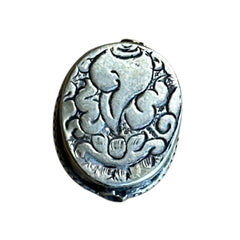 A vintage Tibetan 'silver' and turquoise bead from the 1990s, featuring a turquoise-green oval cabochon with natural matrix, set in a handcrafted bezel. The back of the bead displays intricate repousse work with swirling cloud and flower designs, iconic in Tibetan jewelry.