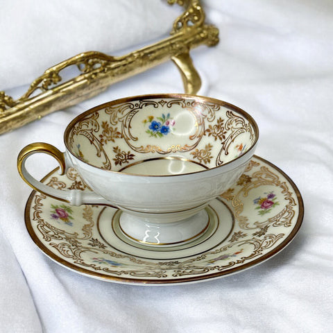 Vintage Tirschenreuth Bavaria demi-tasse and saucer set in cream porcelain with ornate floral clusters and gold scrollwork; footed teacup with gilded handle and rim, saucer marked with crown and shield logo and red glaze number 2284.