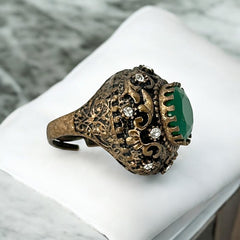 Vintage 1990s Turkish Sultan-style adjustable ring featuring a faceted emerald glass cabochon, clear rhinestones, and ornate antiqued bronze detailing in very good condition.