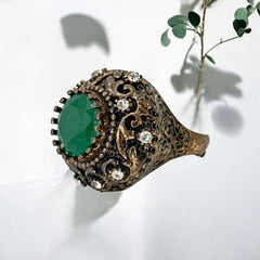 Vintage 1990s Turkish Sultan-style adjustable ring featuring a faceted emerald glass cabochon, clear rhinestones, and ornate antiqued bronze detailing in very good condition.