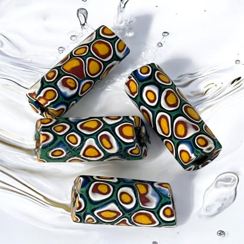 A set of vintage Venetian millefiori African trade beads in vibrant green and yellow. The tube-shaped glass beads, originating from Ghana, feature intricate floral patterns and showcase the rich history of 19th and 20th-century trade. Some beads show minor chips due to age, adding to their authentic vintage charm